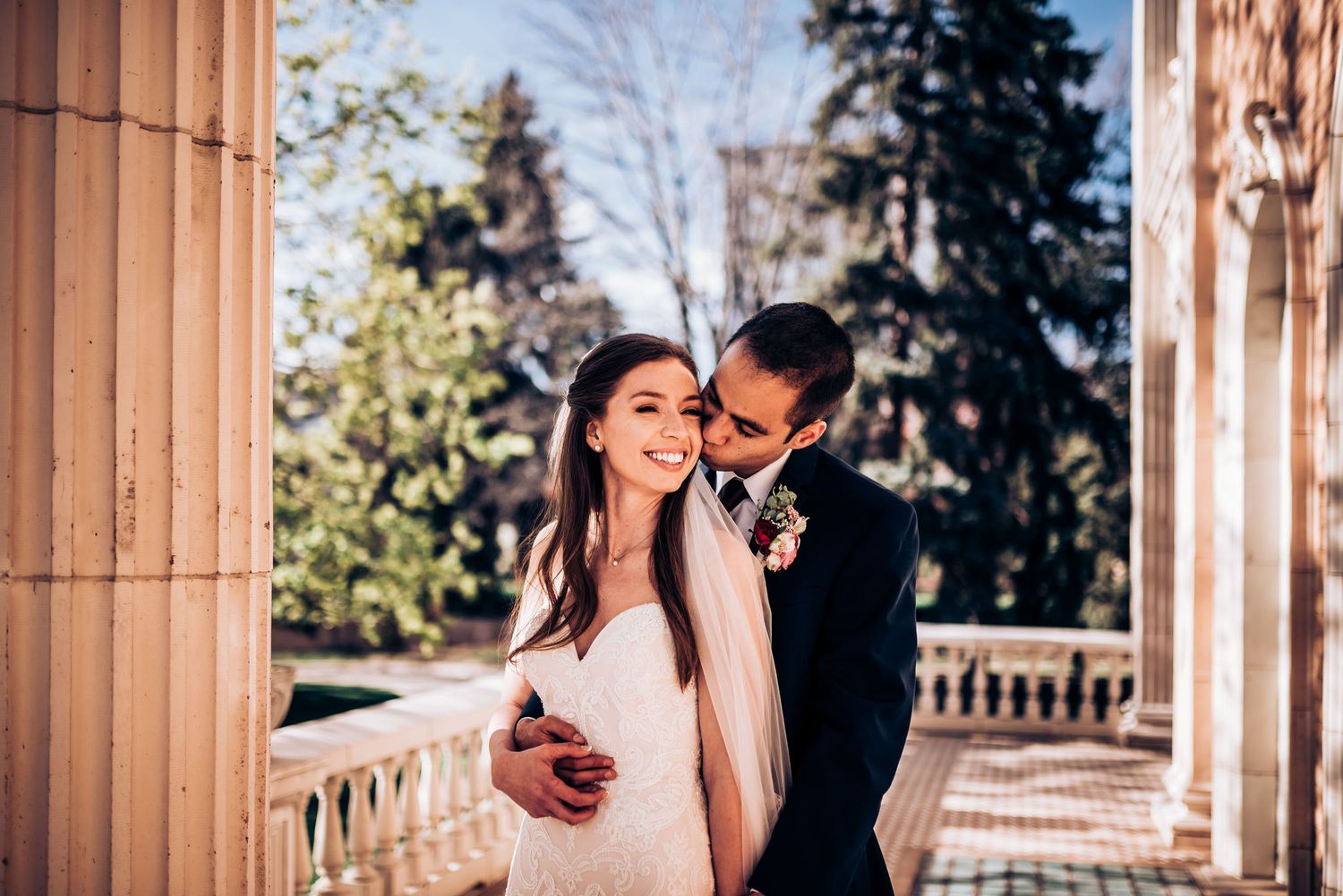 Couple shares intimate moment between ornate columns during outdoor wedding photoshoot.