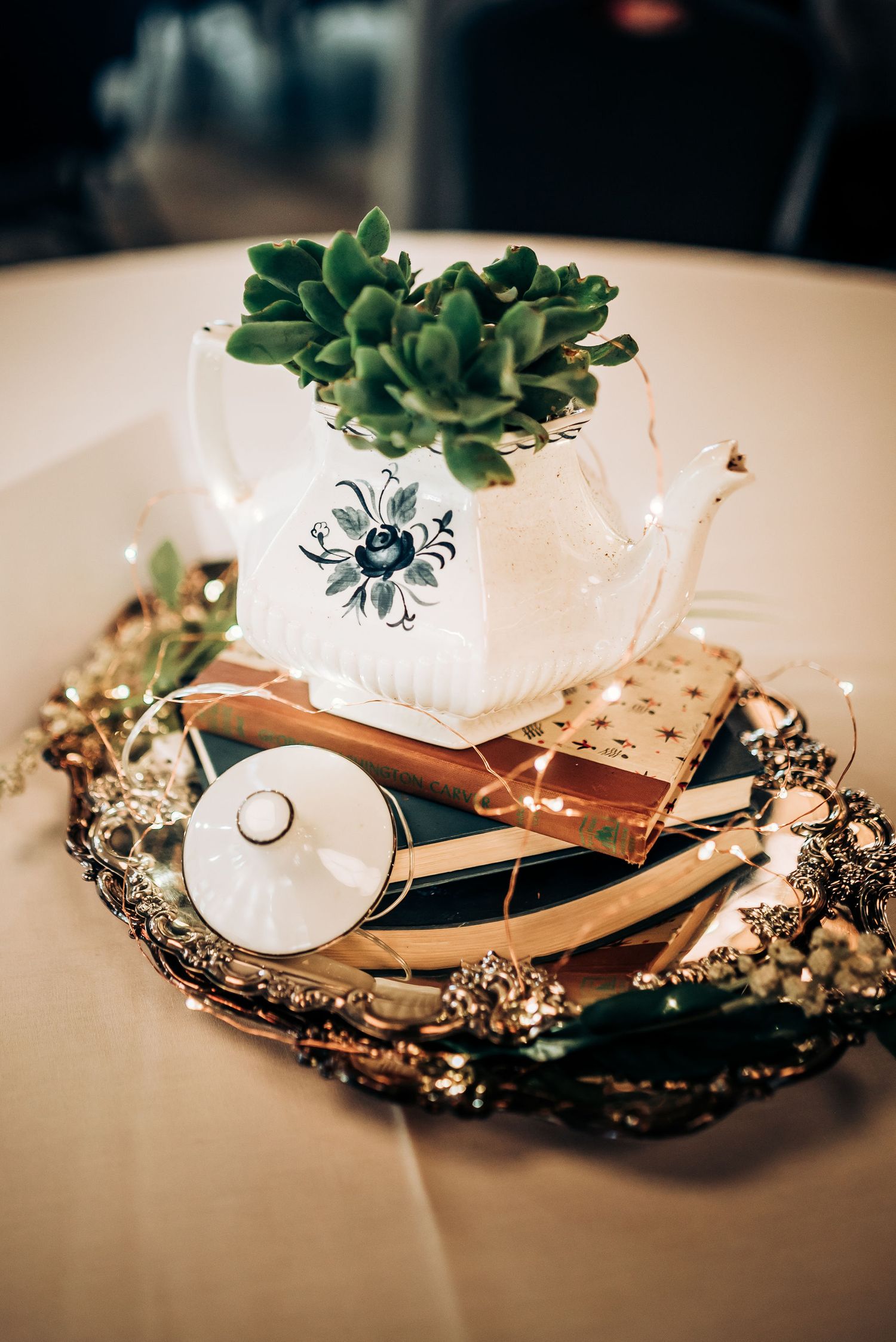 Succulent plant in vintage teacup with decorative elements on ornate tray centerpiece.