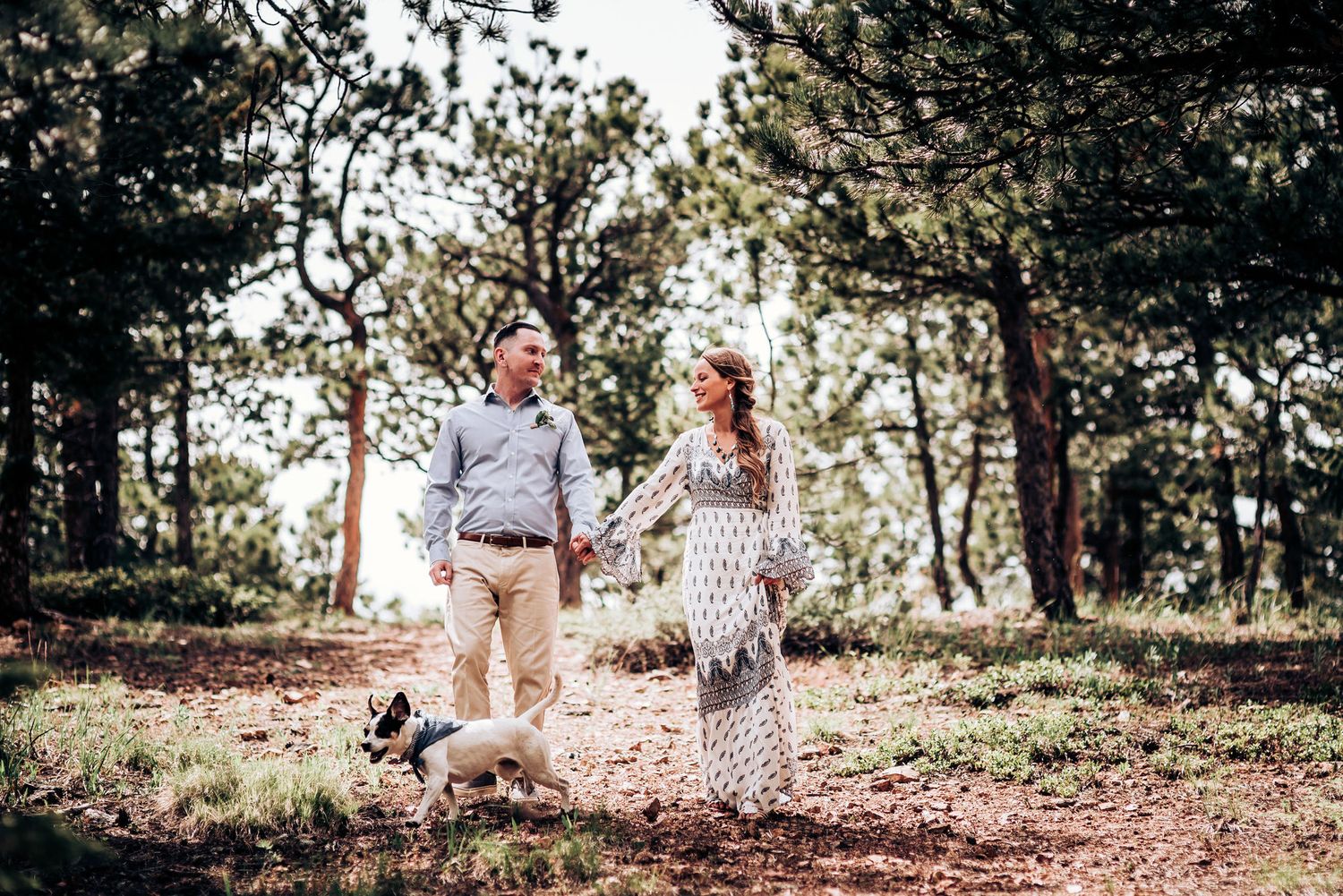 A joyful couple walks together through a pine forest on a sunny afternoon.