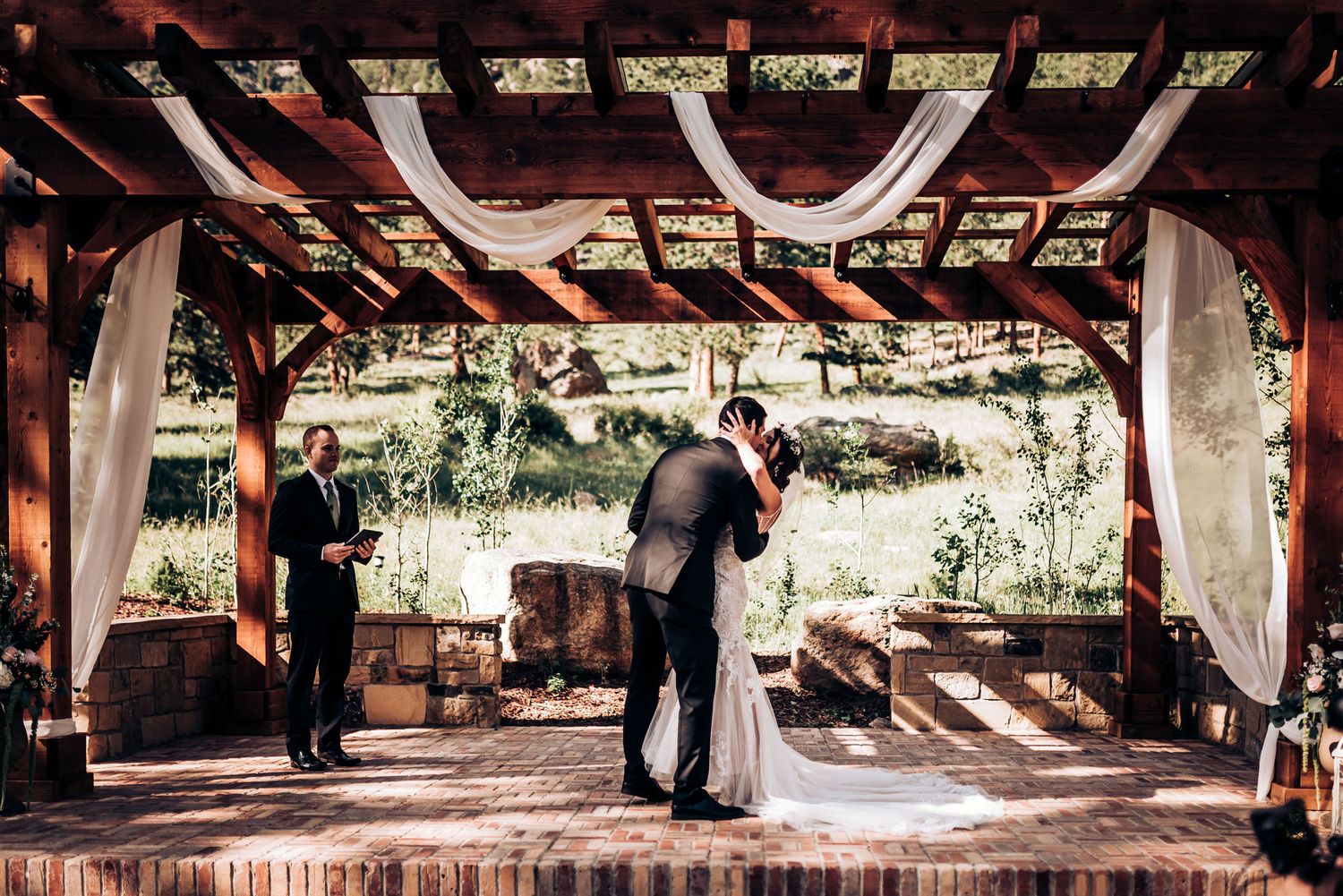 Newlyweds share intimate moment under wooden pavilion decorated with white drapes.