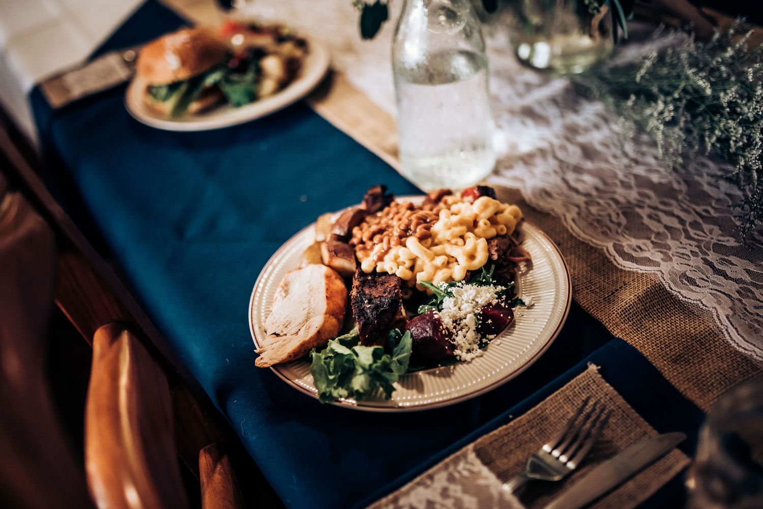 An elegant plated dinner with meat and vegetables served on white dishes with blue tablecloth.