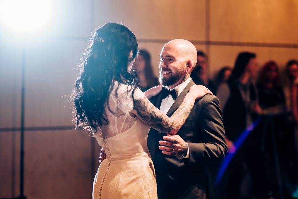 Couple dancing in formal attire under dramatic lighting during wedding reception.