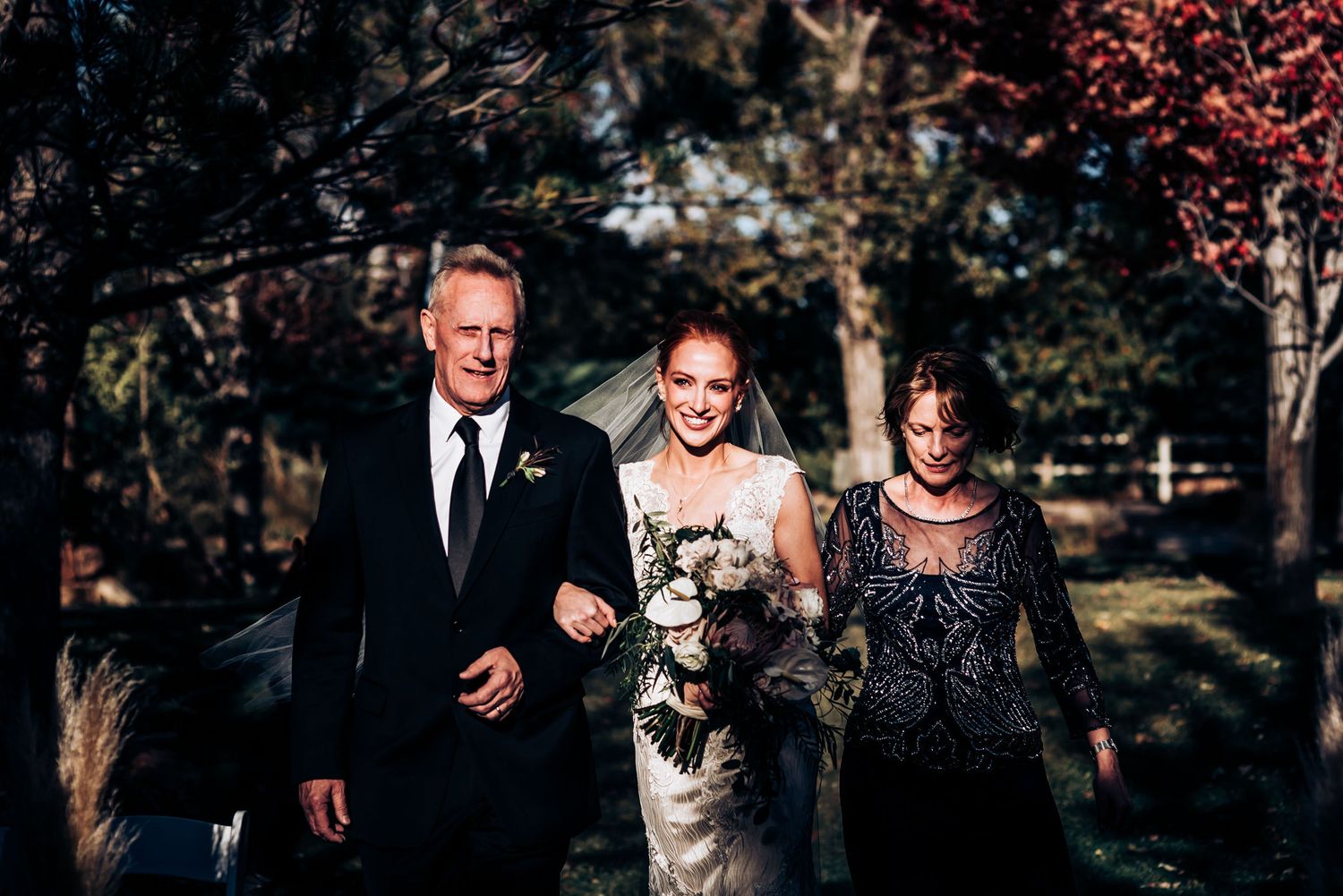 Wedding party members walk together outdoors during a fall ceremony beneath colorful trees.