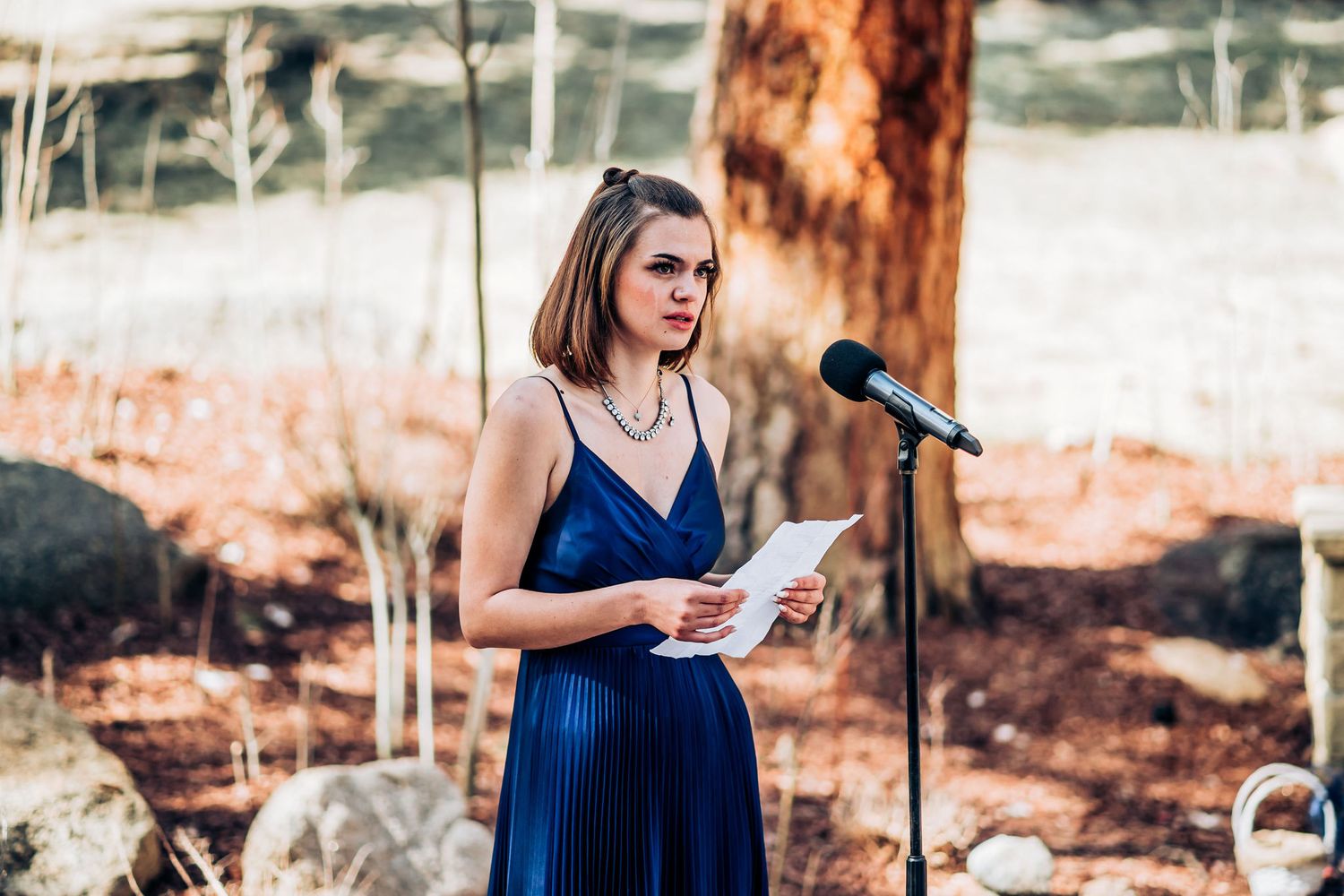 Person in navy blue dress giving speech at outdoor wedding ceremony.