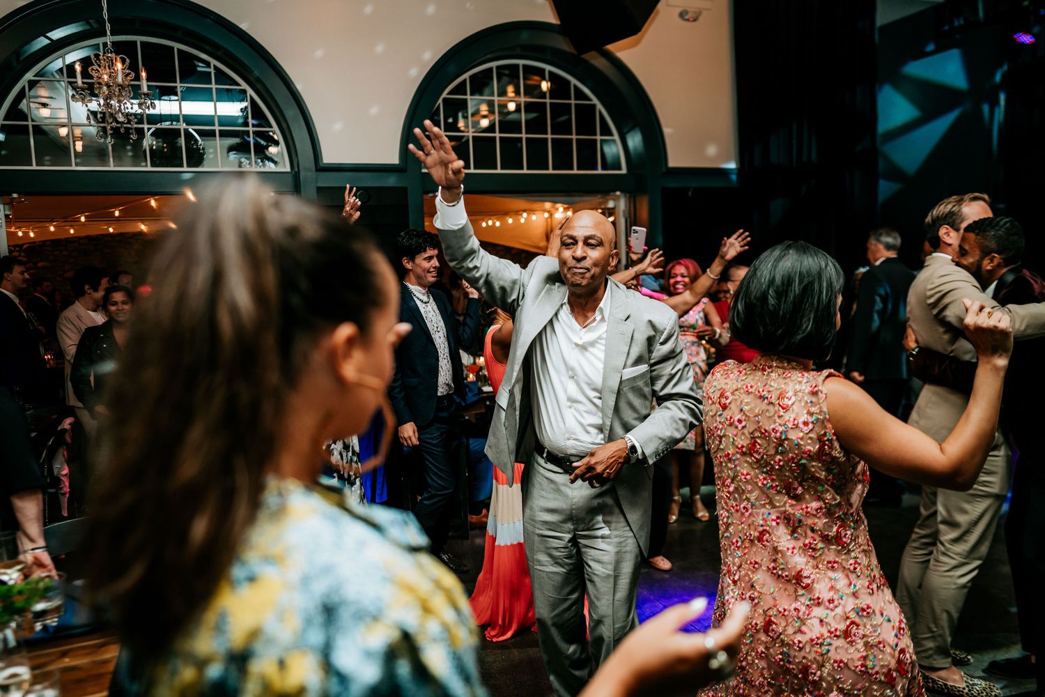 Lively dance floor scene at a wedding reception with guests enjoying themselves under arched windows.