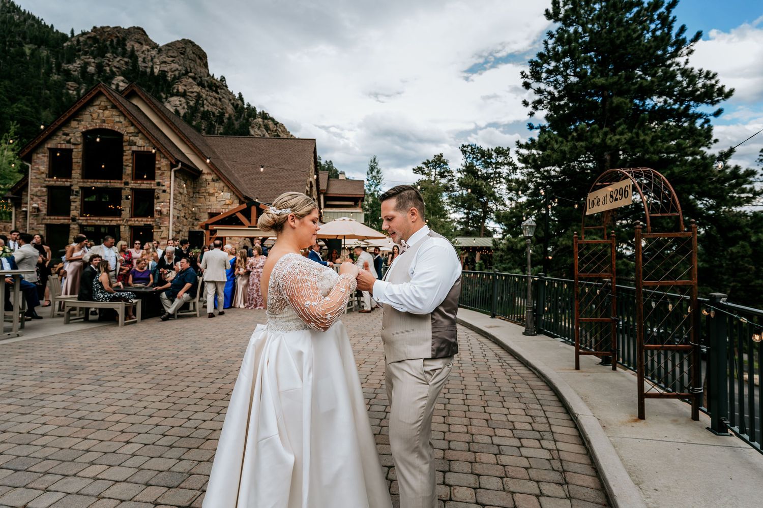A couple dances on a stone patio in front of a rustic mountain lodge with guests looking on.