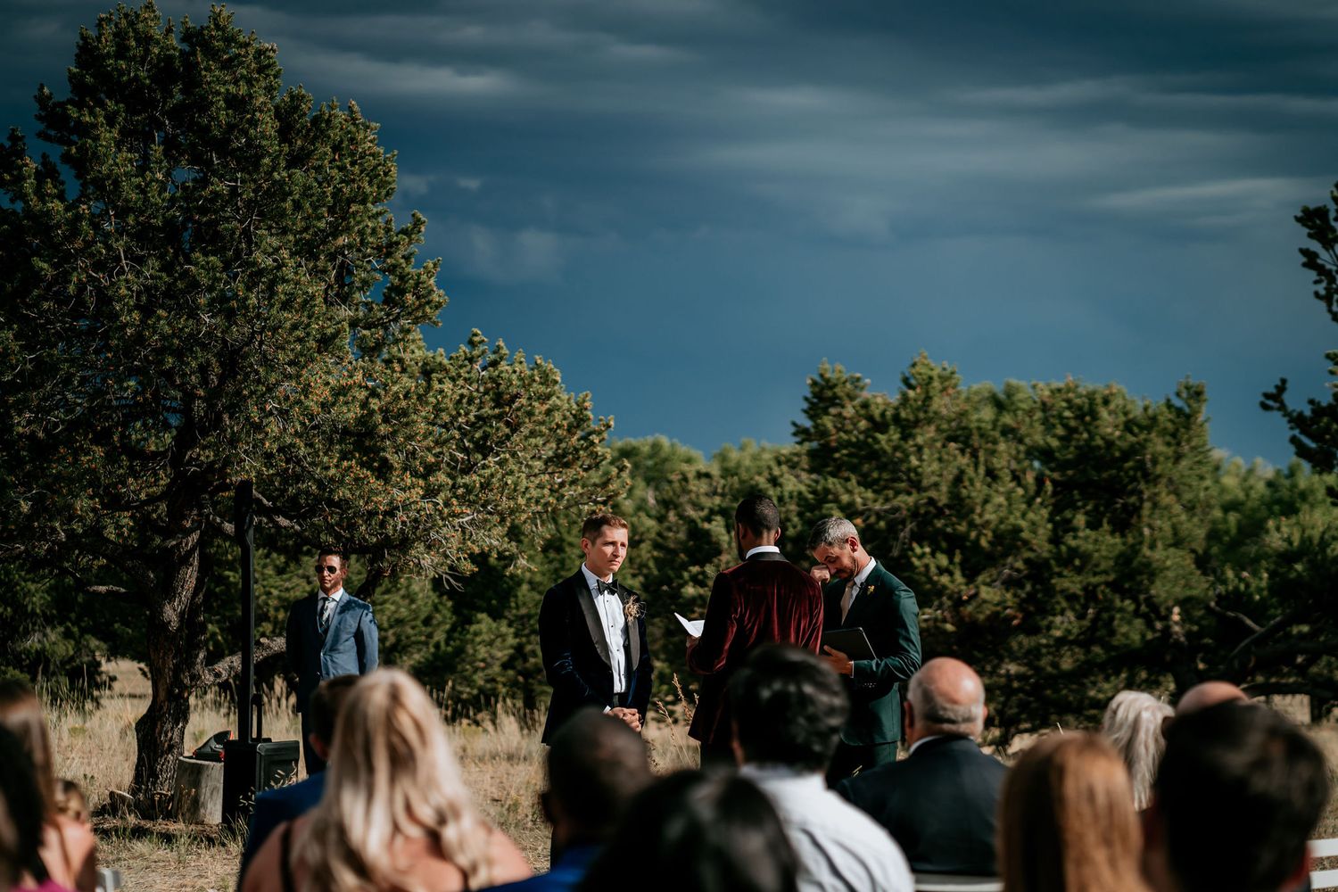 Wedding ceremony in progress under dramatic blue skies with mountain scenery.