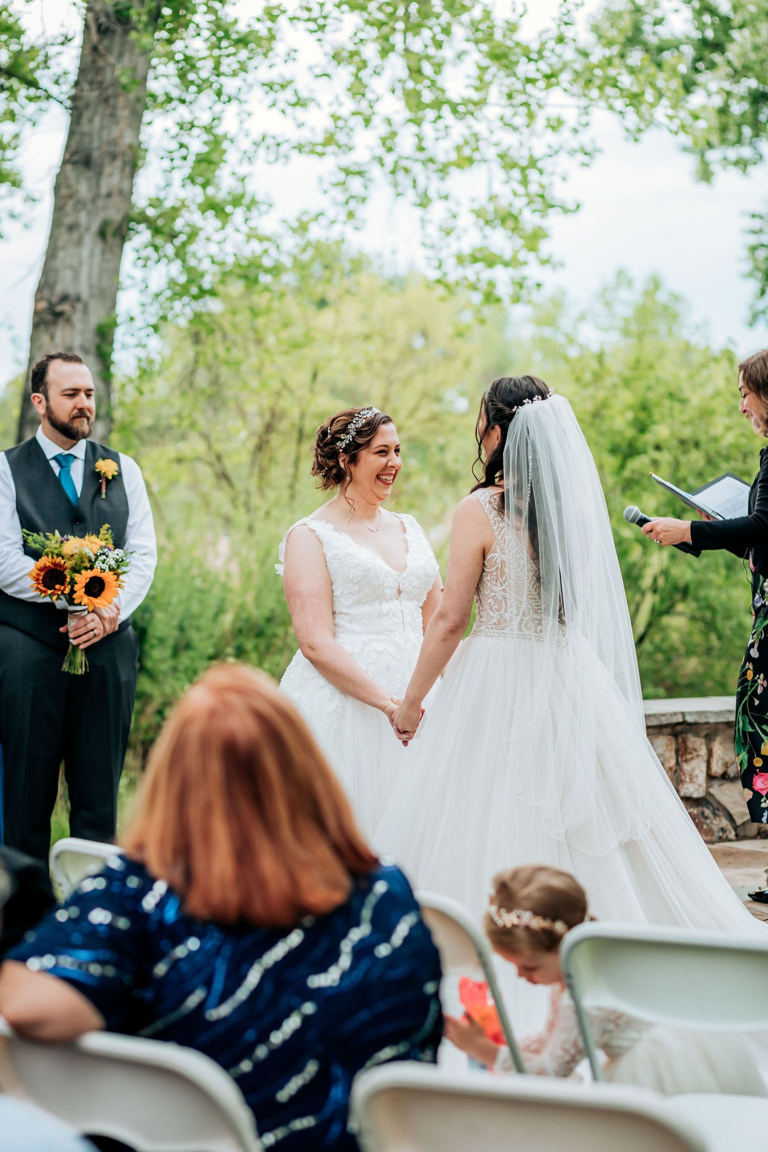 Outdoor wedding ceremony with sunflower bouquet and guests seated.