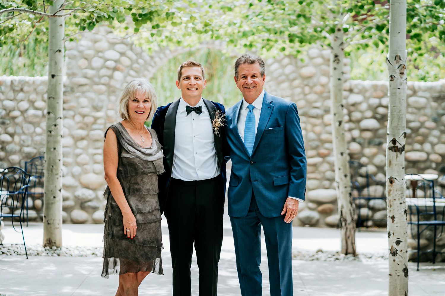 Family group in formal attire posing against stone wall backdrop.