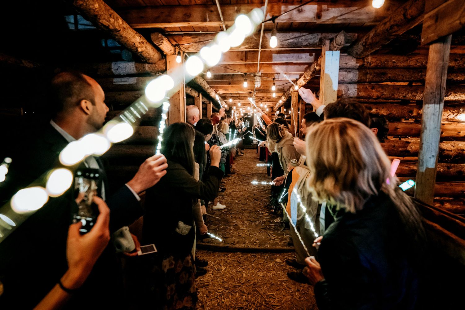 Party guests creating a tunnel of lights in a rustic wooden interior.