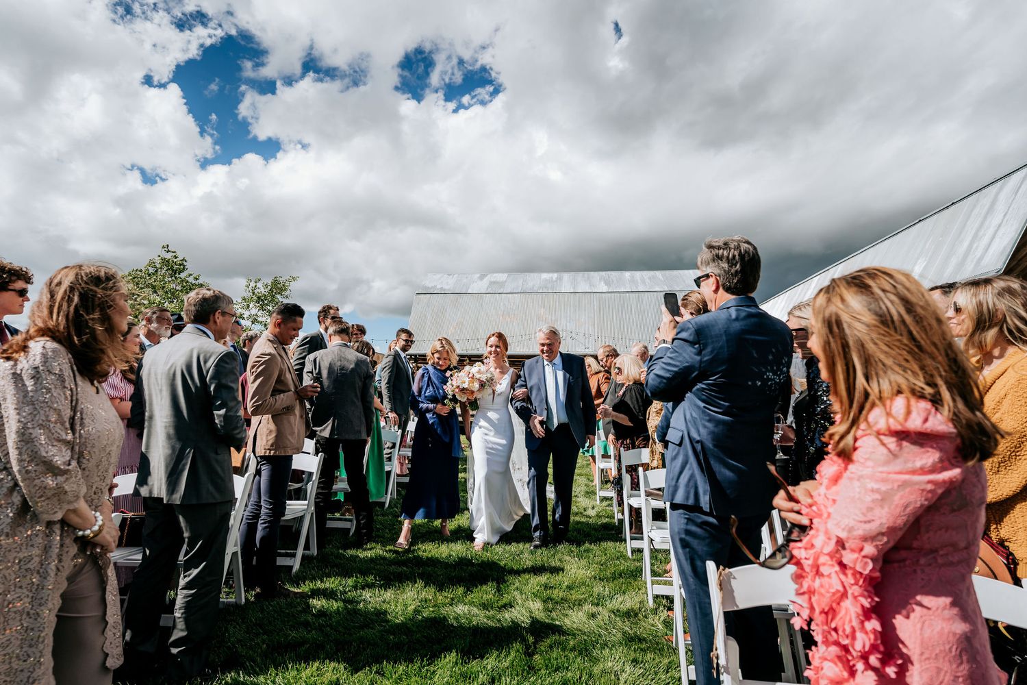 Wedding photographer captures outdoor ceremony with guests and mountain scenery.