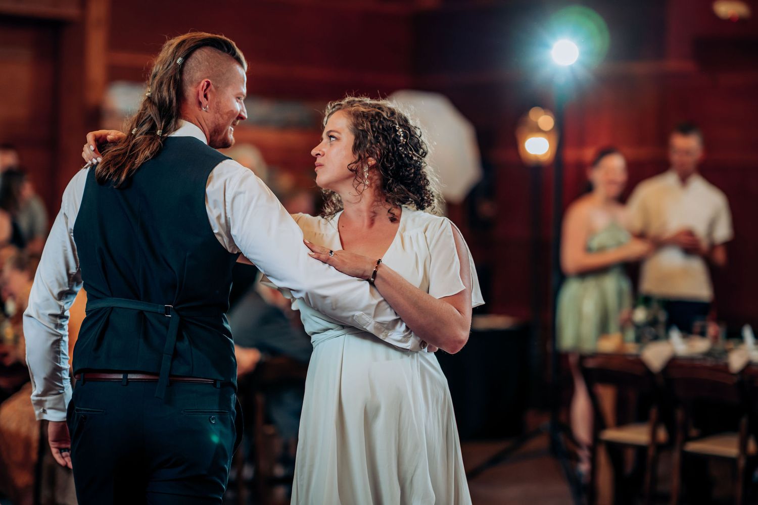 Couple dancing together during a wedding reception in a rustic indoor venue with mood lighting.