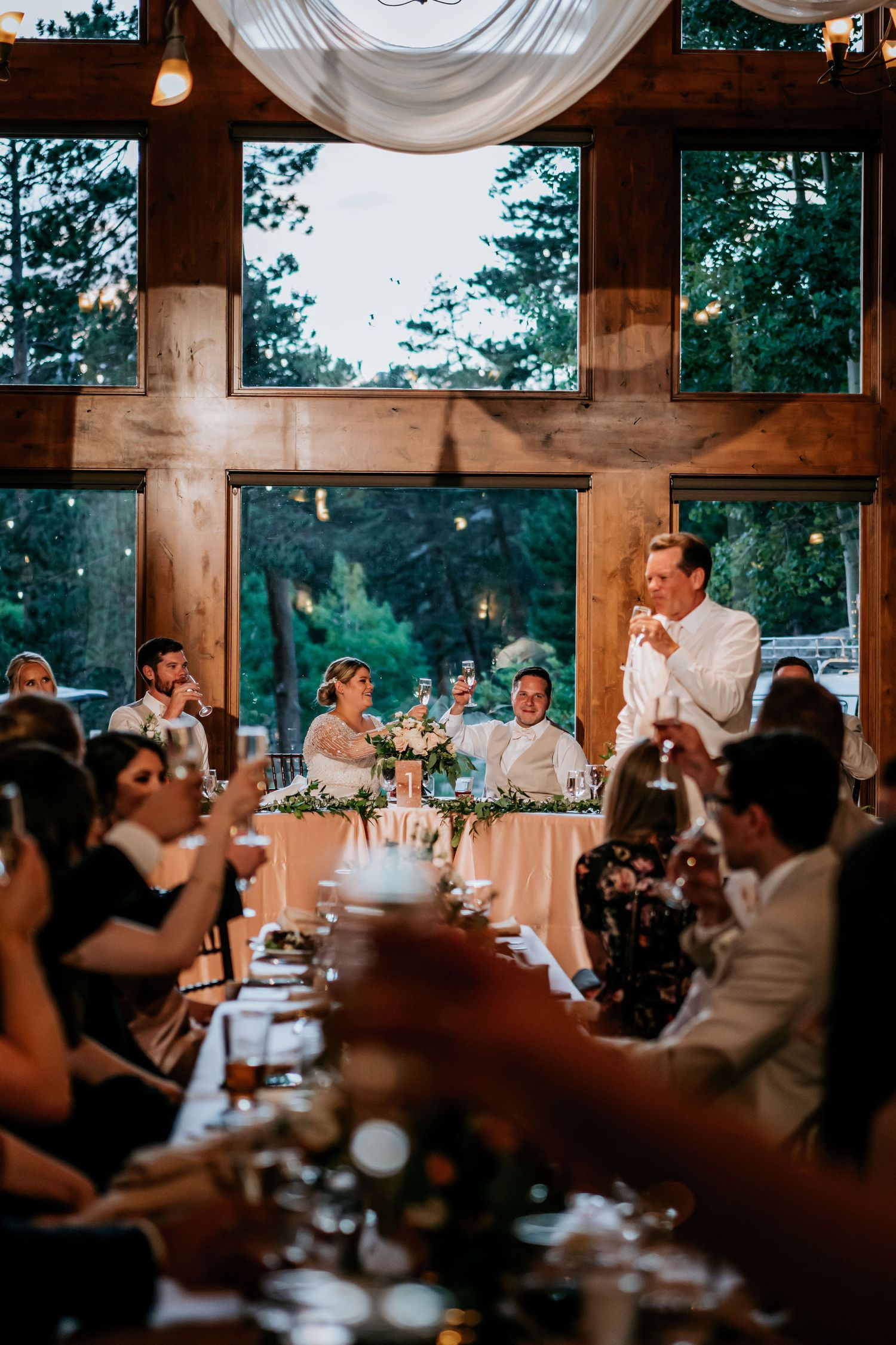 Wedding reception dinner in rustic wooden venue with high ceiling and dramatic lighting.