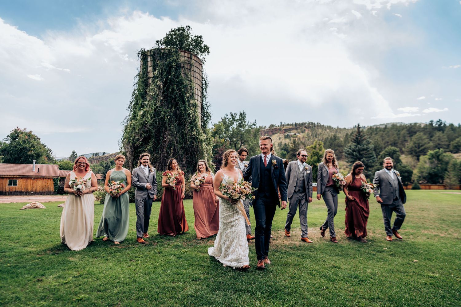 Wedding party arranged in casual formation with rustic silo backdrop during outdoor celebration.