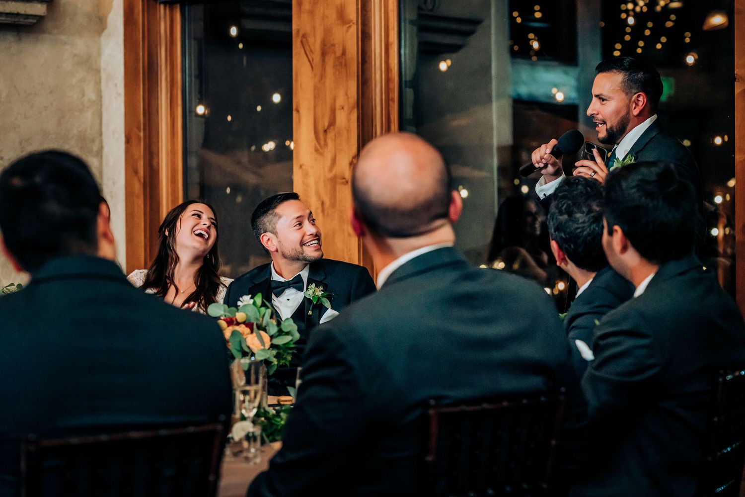 Guests laugh and enjoy speeches during an evening wedding reception.