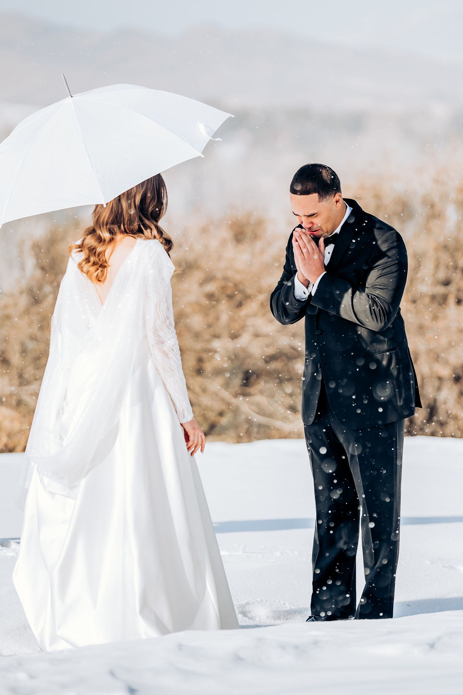 A winter wedding first look moment captured in the snow with mountains in the background.