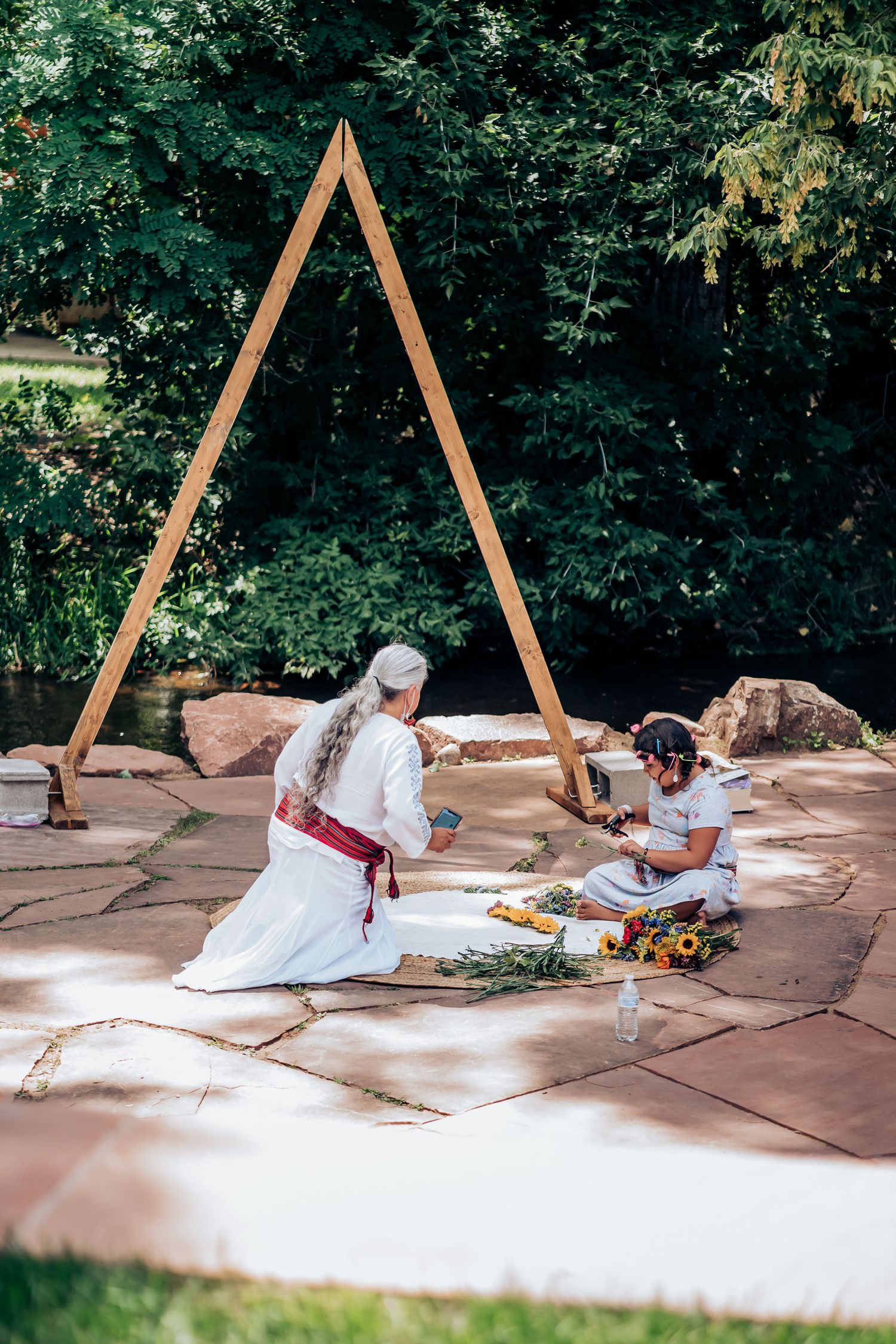 Ceremonial setup under wooden triangle arch with items laid out on stone patio.