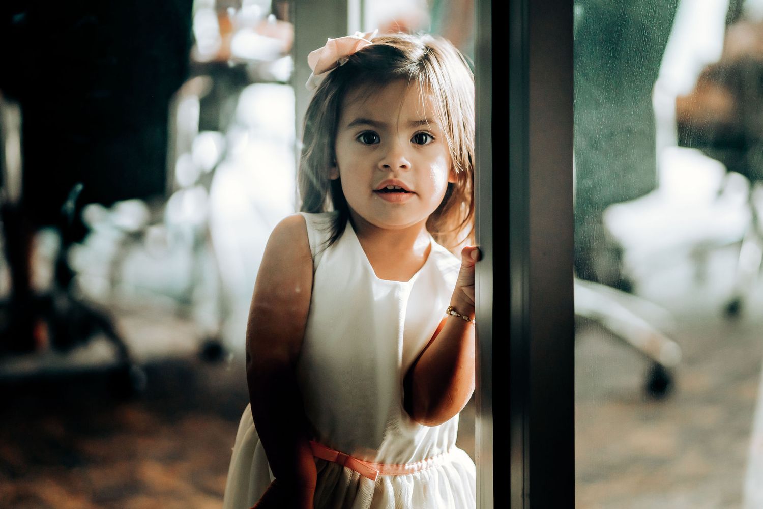 Young child in white dress peeking around a corner.
