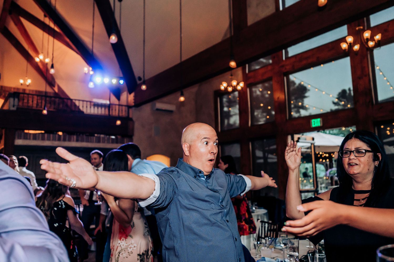 Guests dancing energetically during a wedding reception in a venue with large windows.