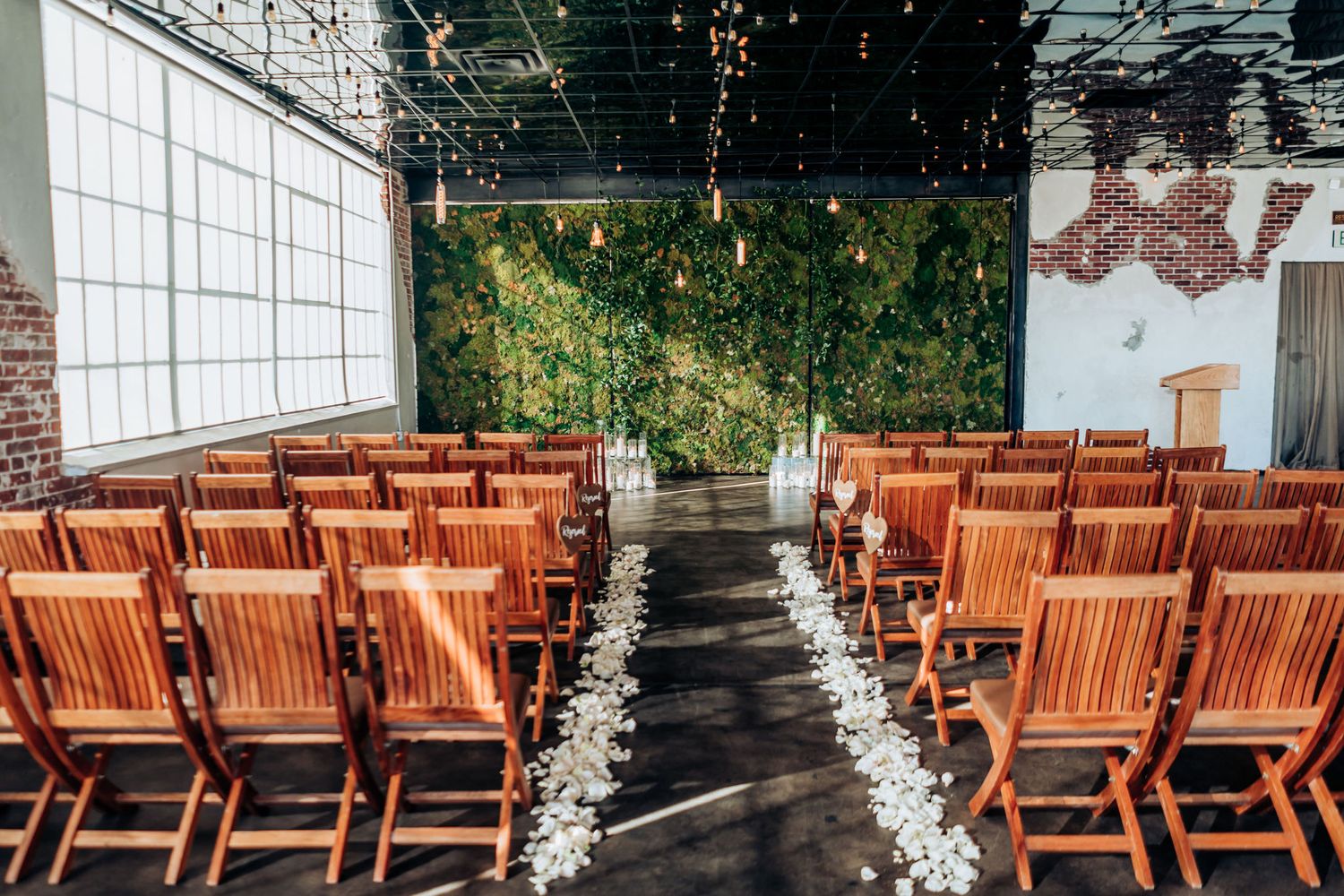 Indoor wedding ceremony setup with wooden chairs and flower petals lining the aisle.