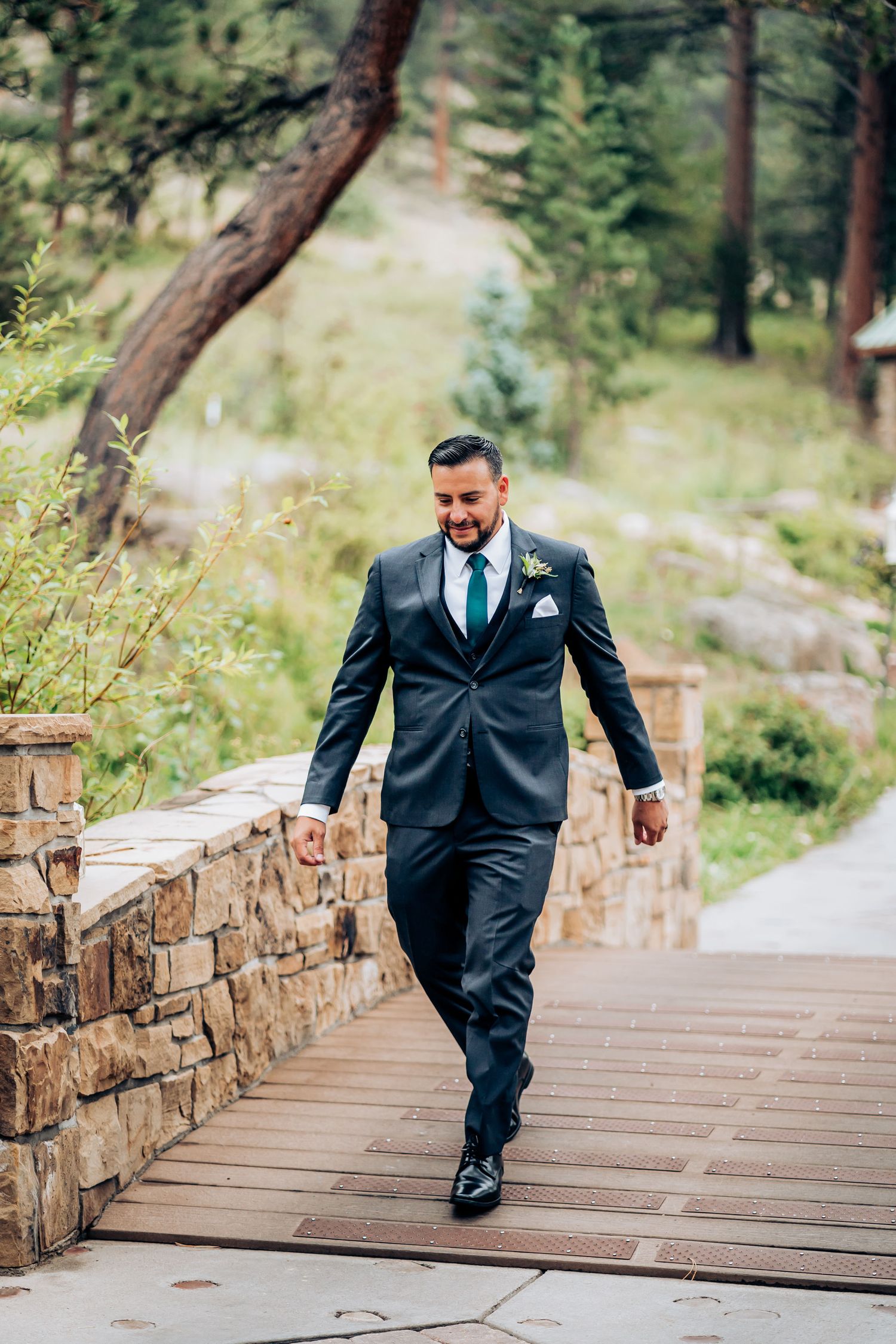 Person in dark suit walking down stone-lined pathway surrounded by mountain scenery.