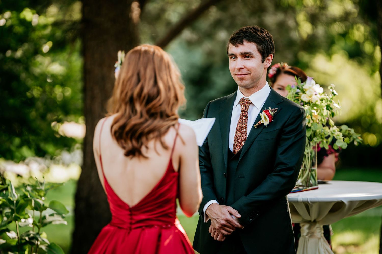 A couple shares a moment during an outdoor ceremony with greenery in the background.