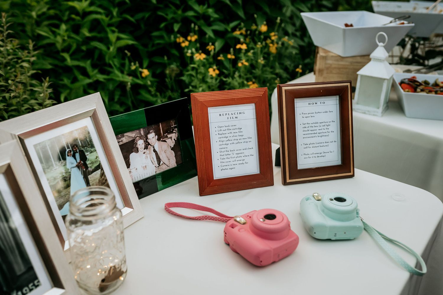 Wedding reception table with framed photos, decorative lanterns, and pink and mint ceramic teapots.