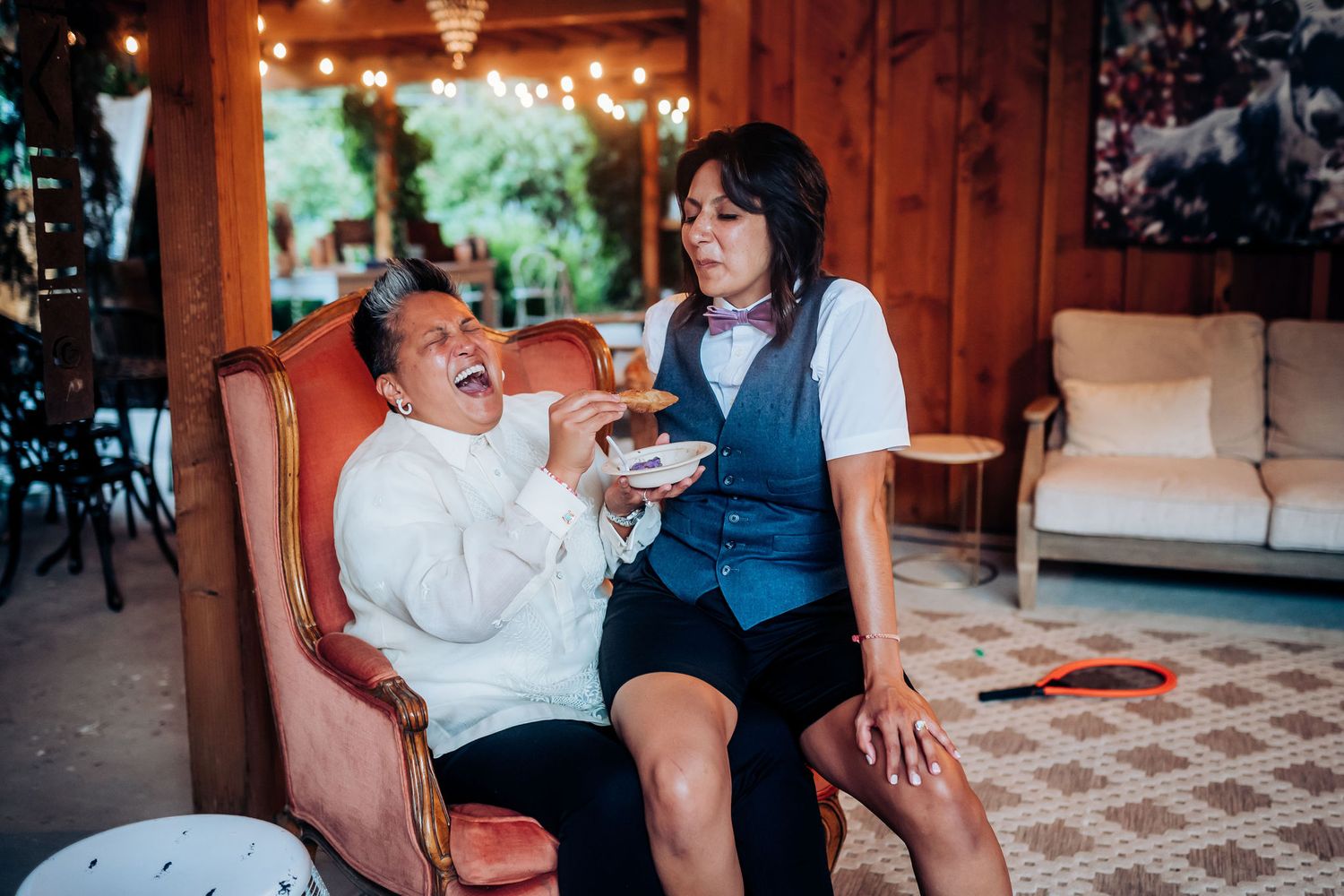 Two people sharing a playful moment on a couch in a rustic indoor setting with string lights.