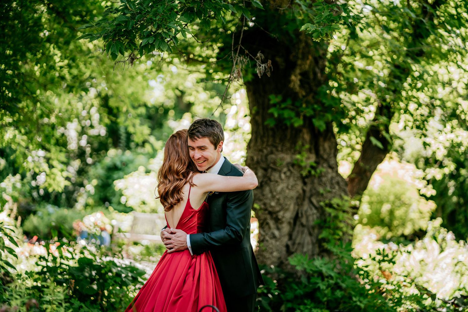 Couple embraces in garden setting with bride wearing striking red gown.