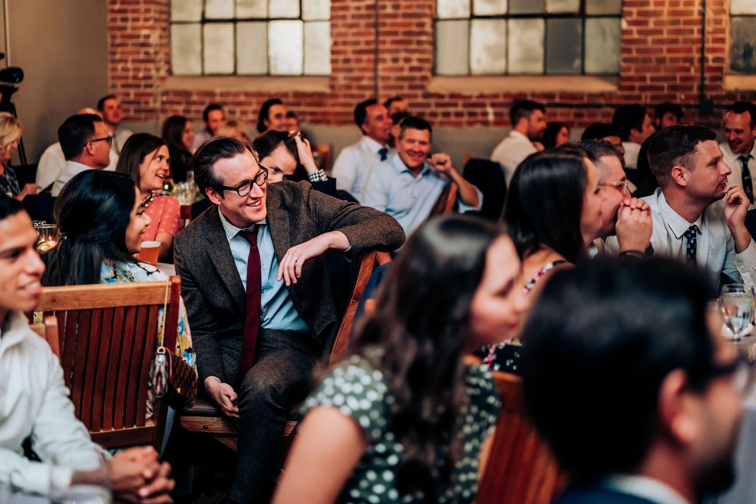 Wedding guests seated in rows of chairs during ceremony in industrial brick venue.