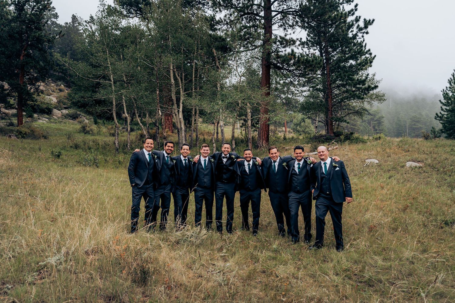 Groomsmen in matching navy suits standing together on a misty mountainside.