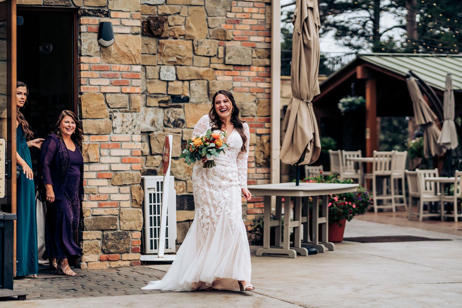 Bride in fitted lace wedding dress poses outside stone building entrance.