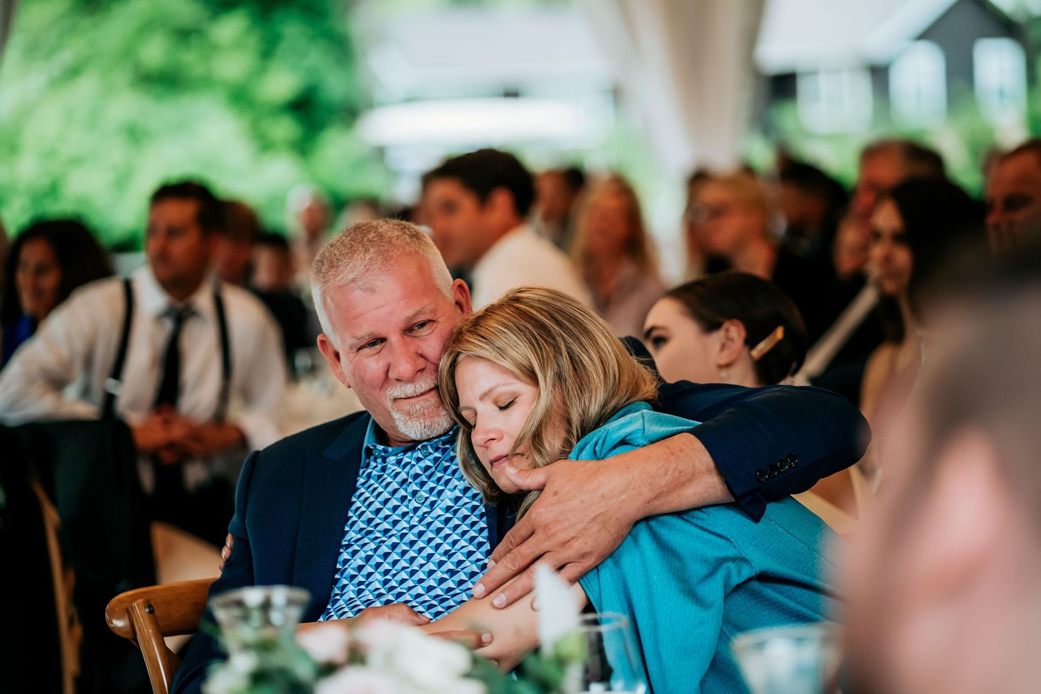 A tender moment between two guests during an outdoor wedding reception under a tent.