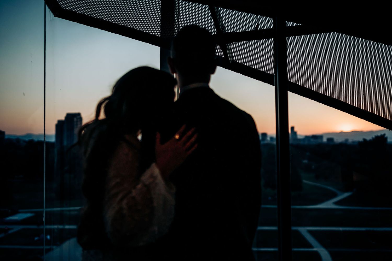Silhouettes of a couple embracing near large windows during sunset in a modern building.