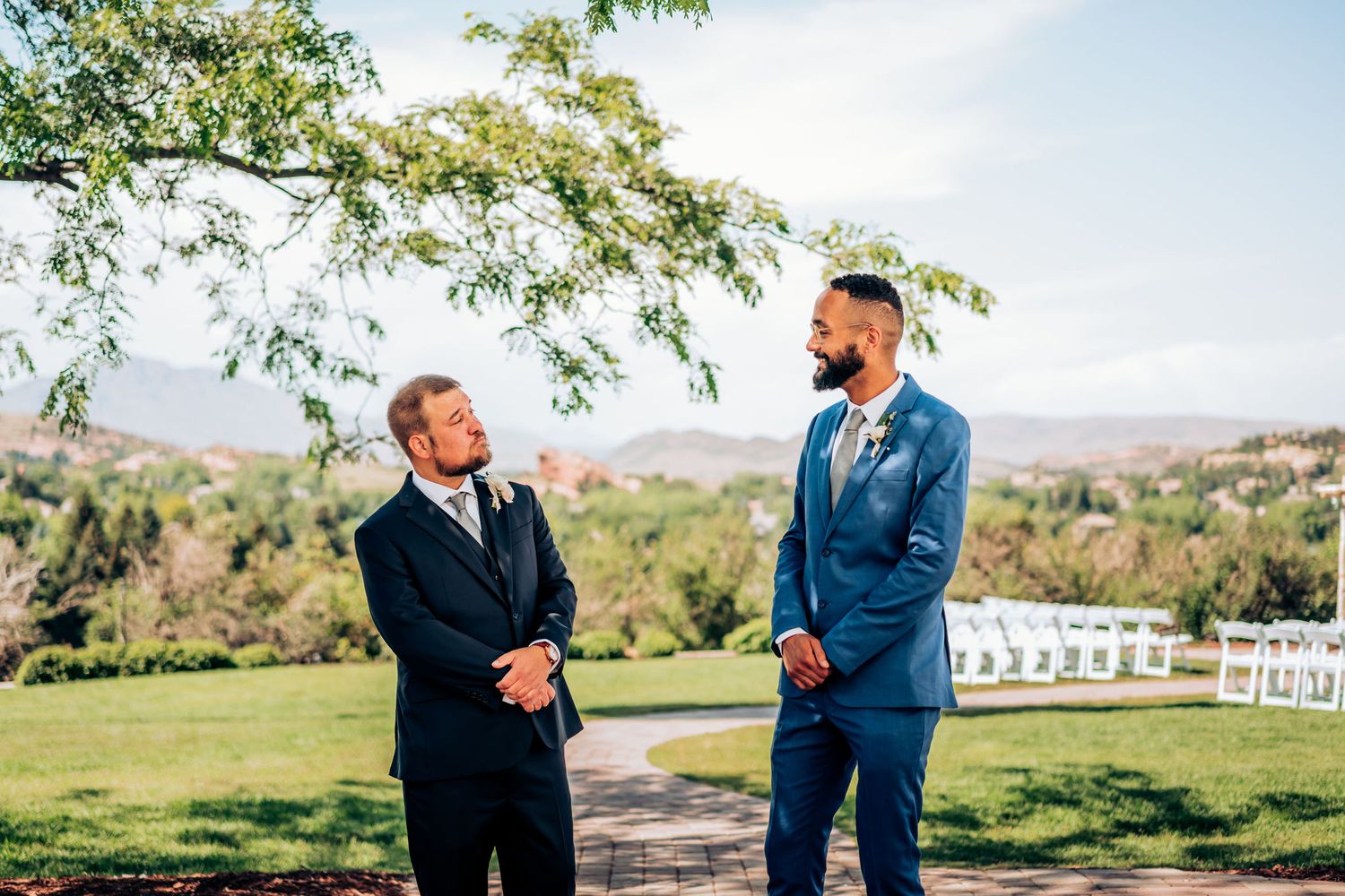 Two men in formal attire having a conversation outdoors at wedding venue.