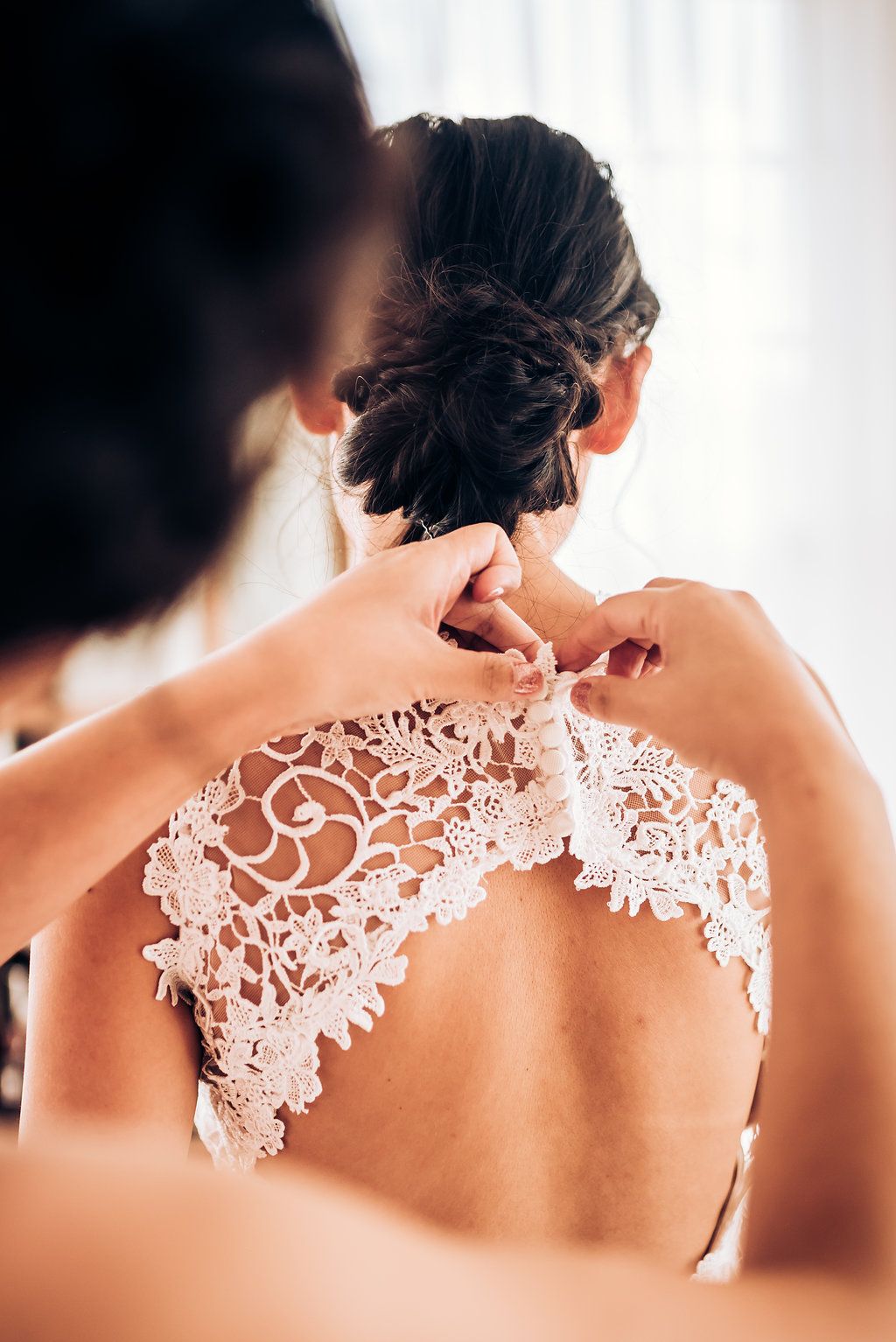 Close-up of intricate lace detail on back of wedding dress being fastened.