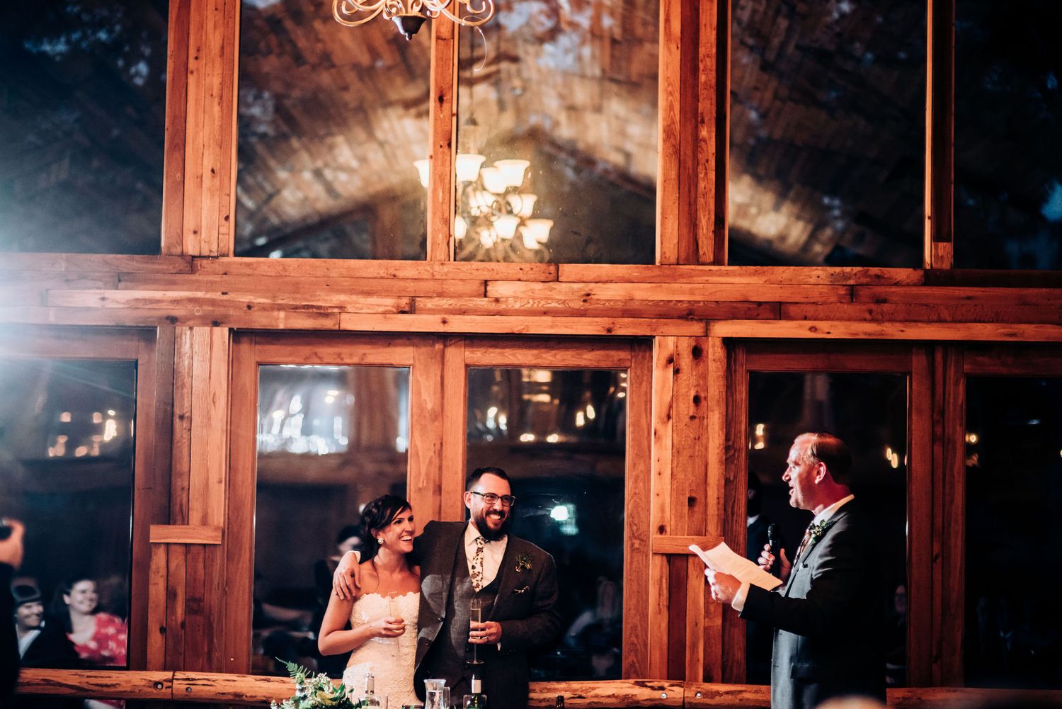Wedding ceremony in a rustic wooden lodge with large windows and hanging lights.