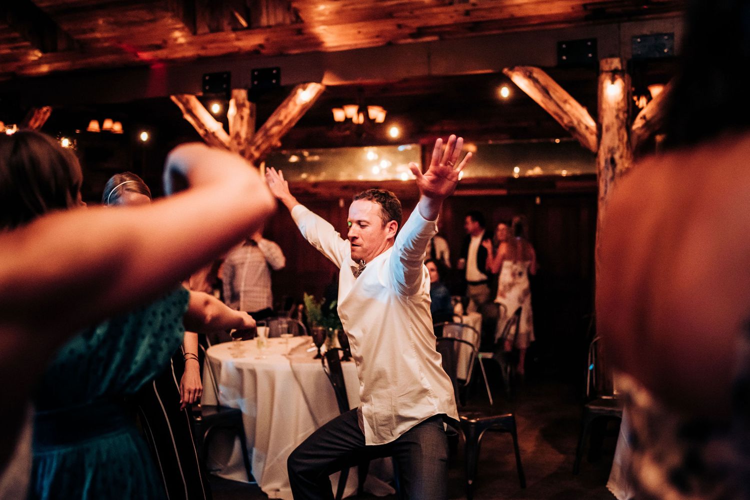 Young guest jumping with excitement on dance floor at indoor wedding reception.