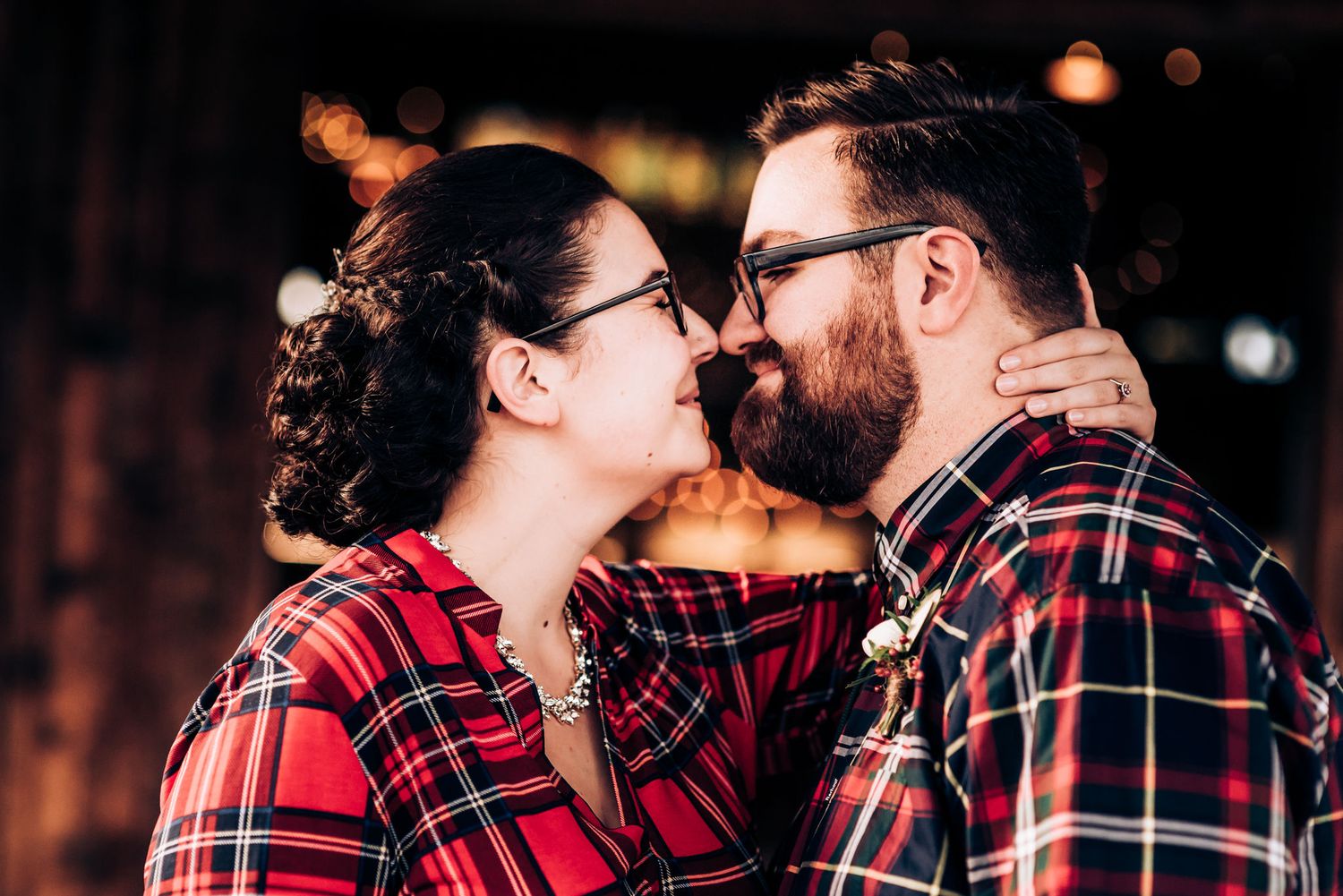 Intimate moment between couple in matching red plaid shirts during golden hour.