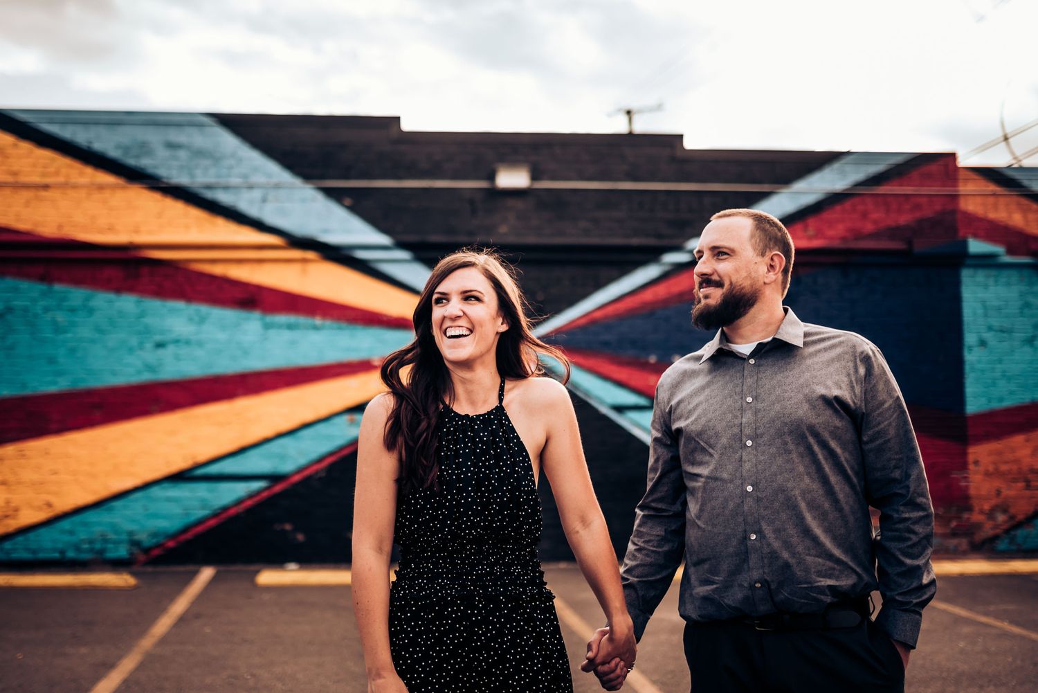 A couple laughs together in front of a vibrant geometric street art mural.