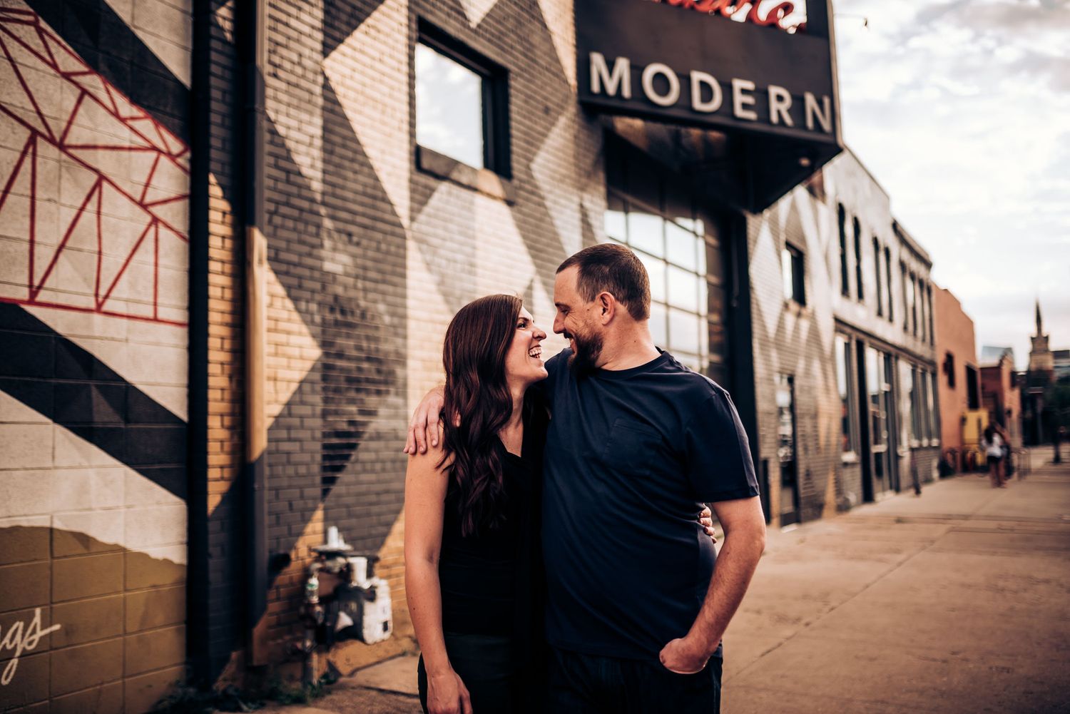 A couple shares a romantic moment outside a modern urban building.