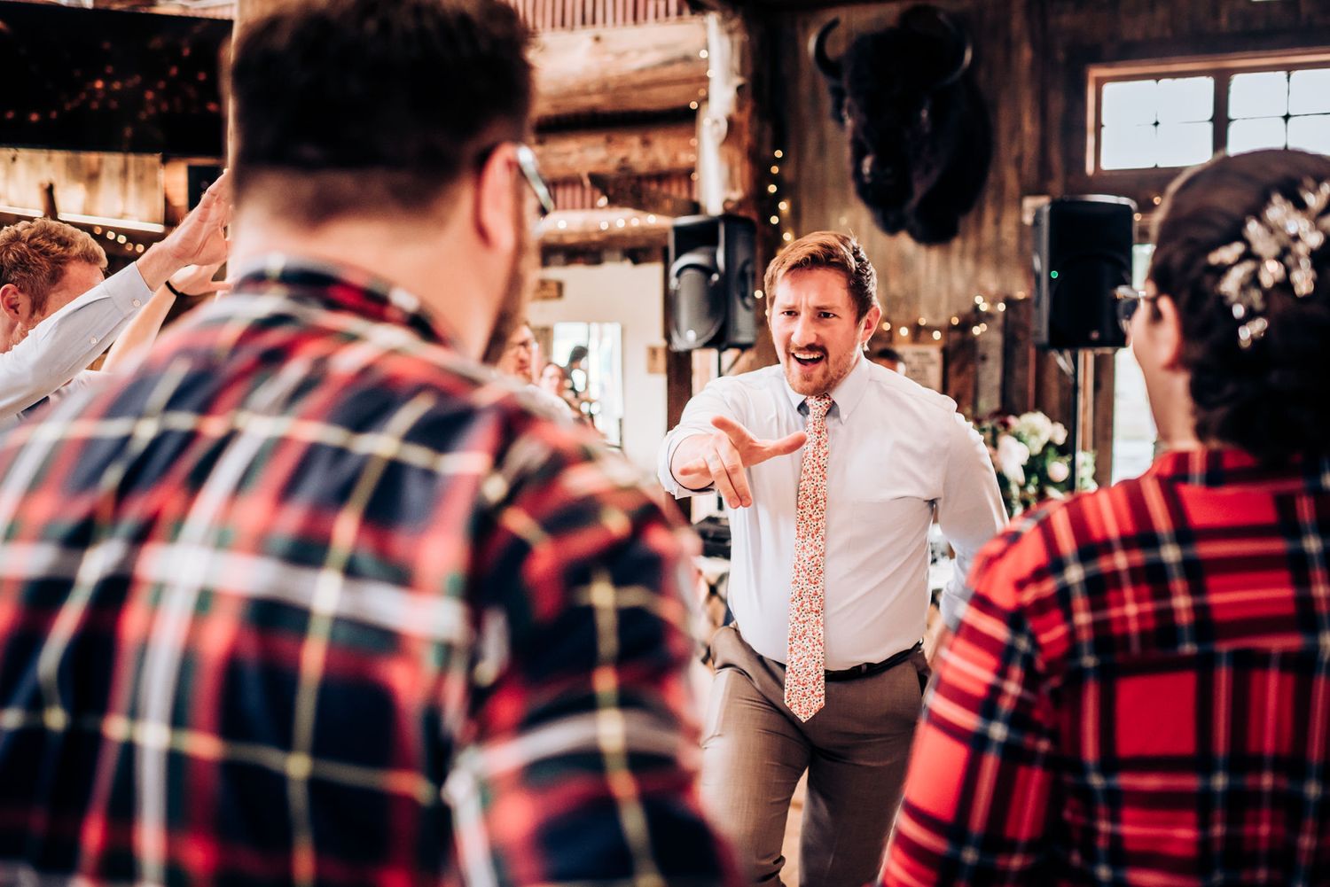 Guests in plaid shirts watch speech during rustic barn celebration.