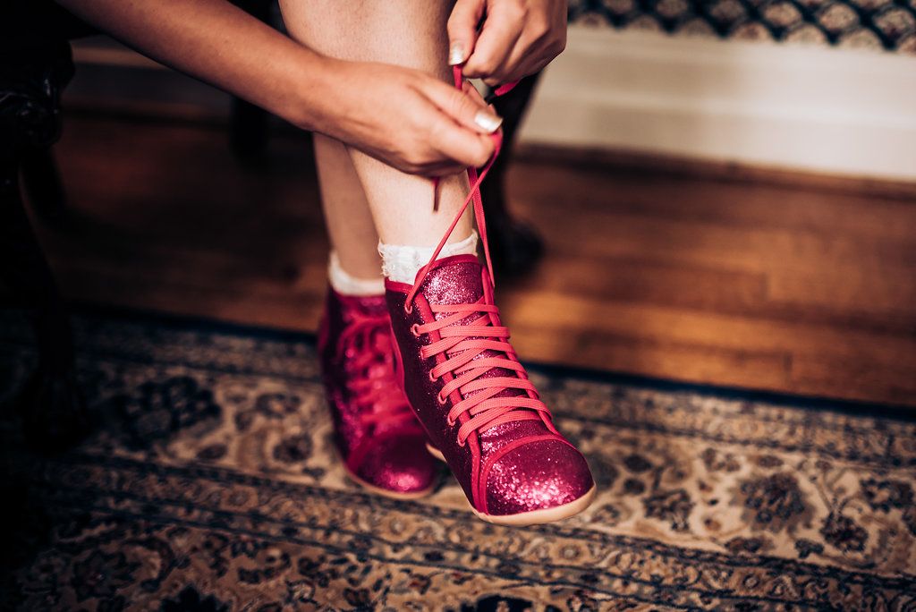 Hands tying bright red sneakers on ornate patterned carpet.
