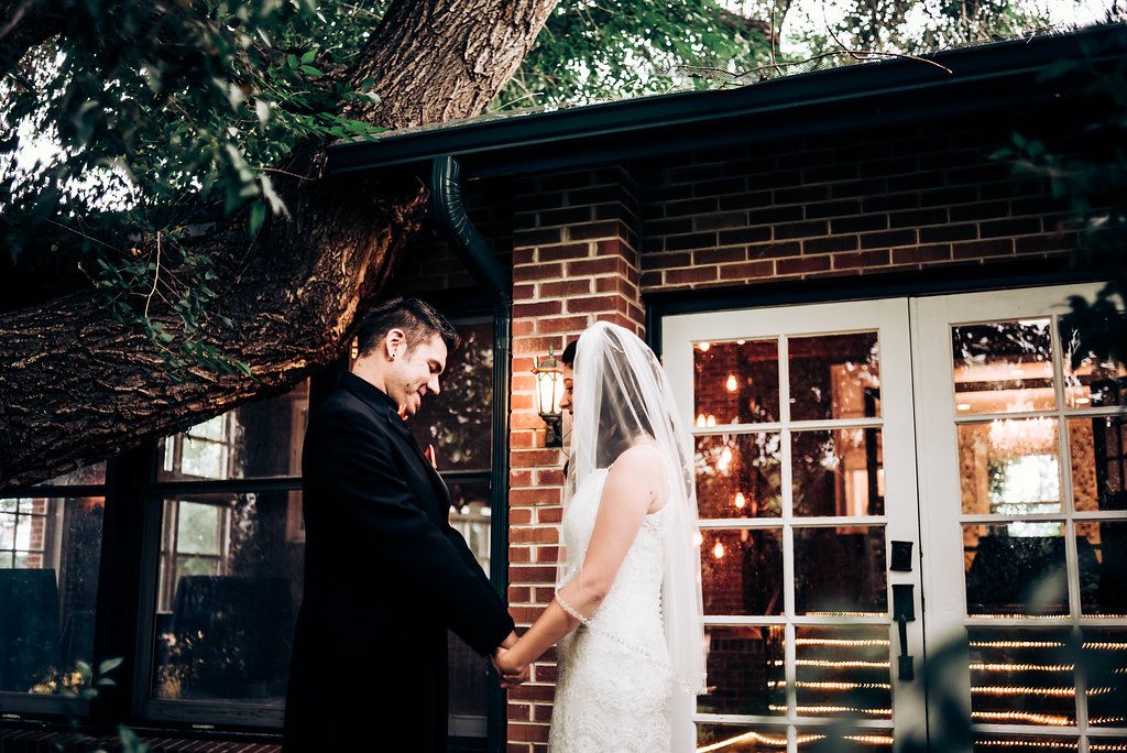 An intimate wedding moment captured in front of a brick building with white french doors and natural foliage.