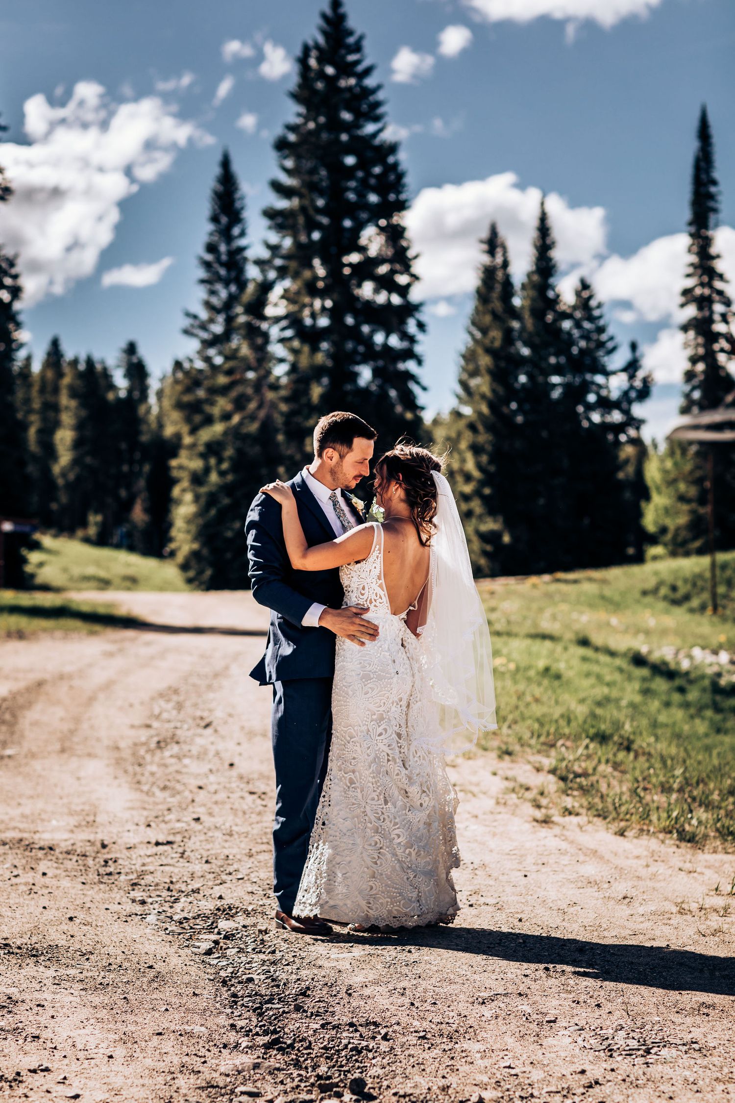 A romantic wedding moment captured on a mountain trail with evergreen trees in the background.