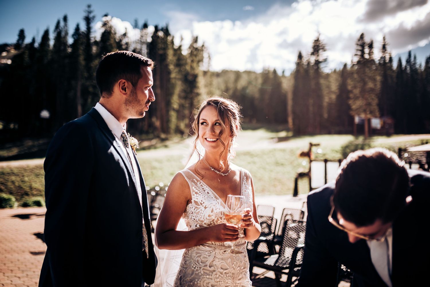 Outdoor mountain wedding ceremony with evergreen trees in golden sunlight.