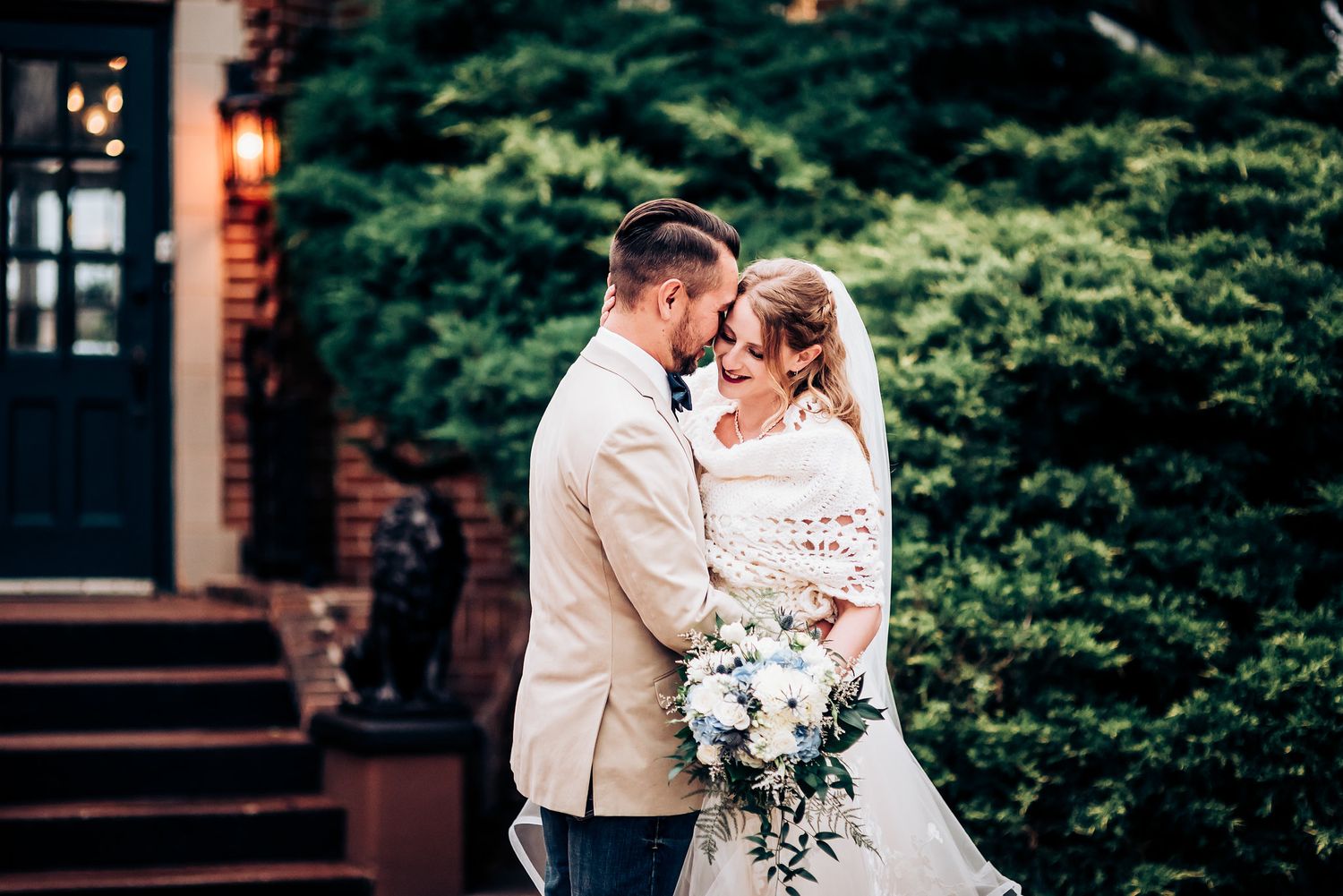 Elegant wedding portrait with lush greenery and brick architecture background.