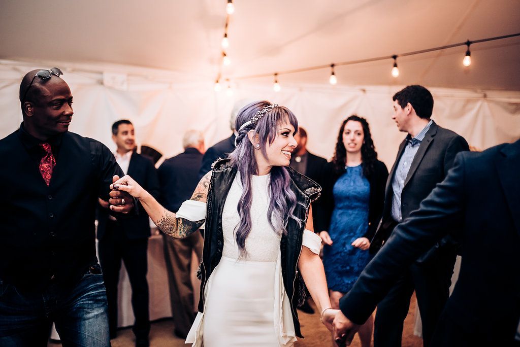 A couple dances together at a wedding reception under string lights with guests in the background.