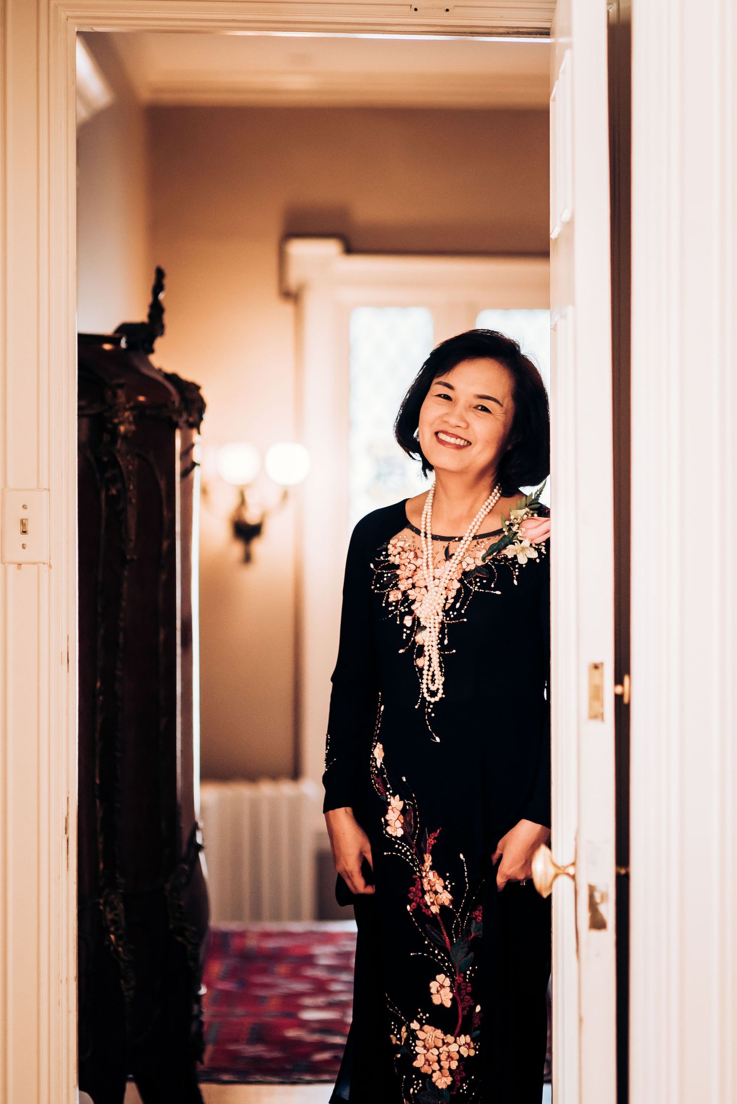 An elegant woman in a floral embroidered black dress standing in a doorway.
