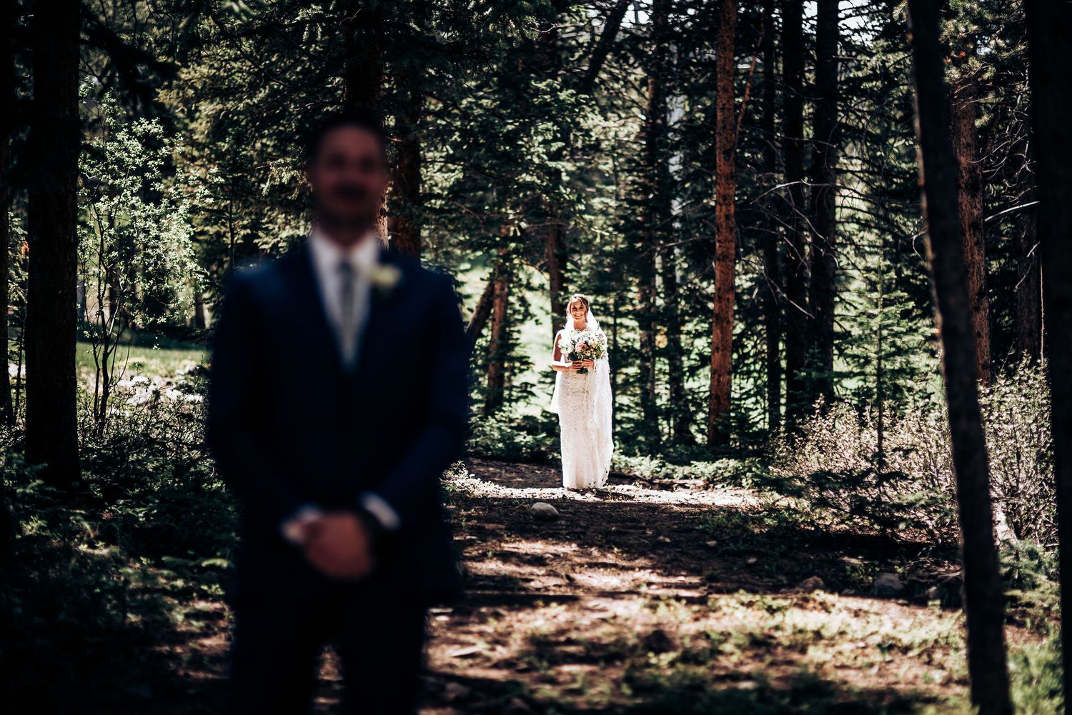 A couple shares their first look moment in a sunlit forest setting during their wedding ceremony.